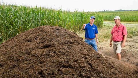 Two people stand next to a pile of soil